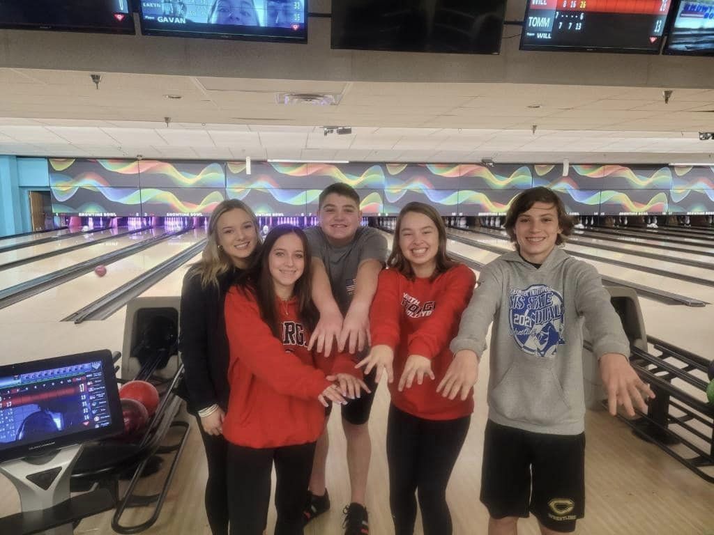 5 students standing in front of bowling lane holding hands out in front of them