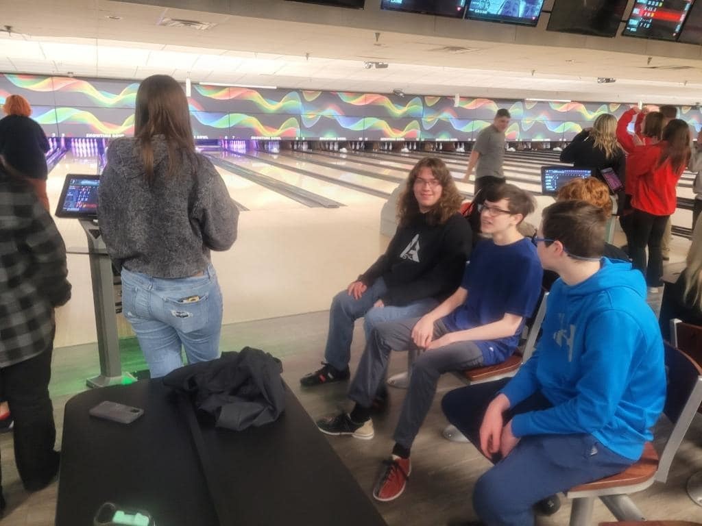 3 students sitting in chairs by bowling lane waiting to bowl 